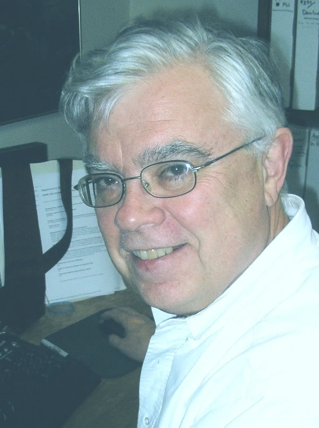 A man with glasses and white hair sitting at a desk.
